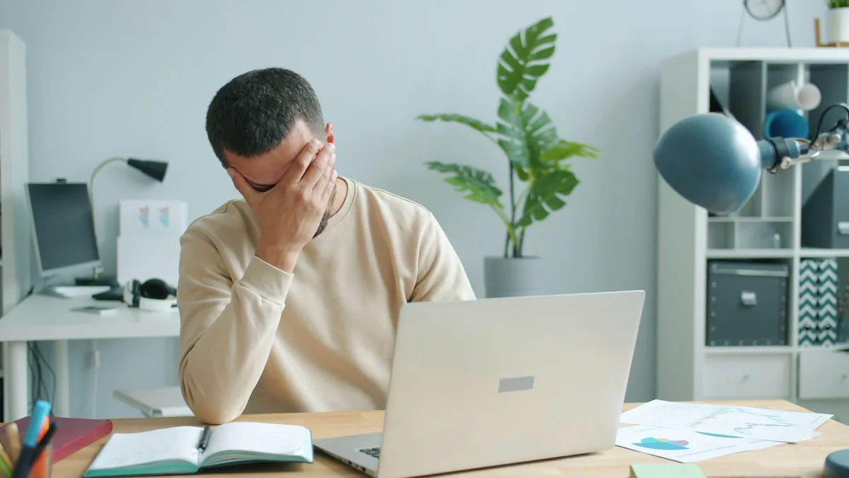 Man with his palm against his face behind a laptop